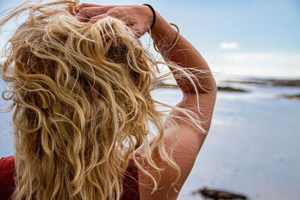 filles blondes de dos qui passe les mains dans les cheveux et regarde la mer