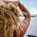filles blondes de dos qui passe les mains dans les cheveux et regarde la mer